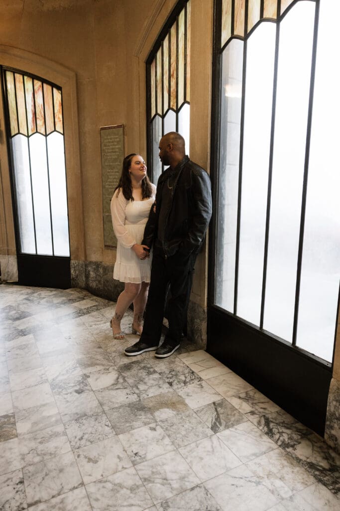 Couple standing by stained glass windows inside Vista House at Crown Point in Corbett, Oregon.
