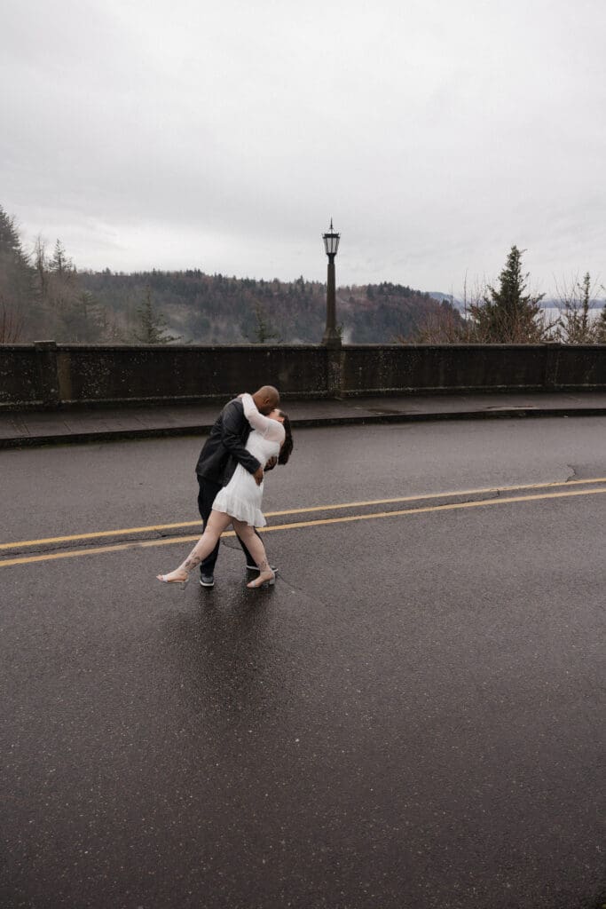 Couple sharing a dip kiss on wet roadway at Vista House at Crown Point in Corbett, Oregon.