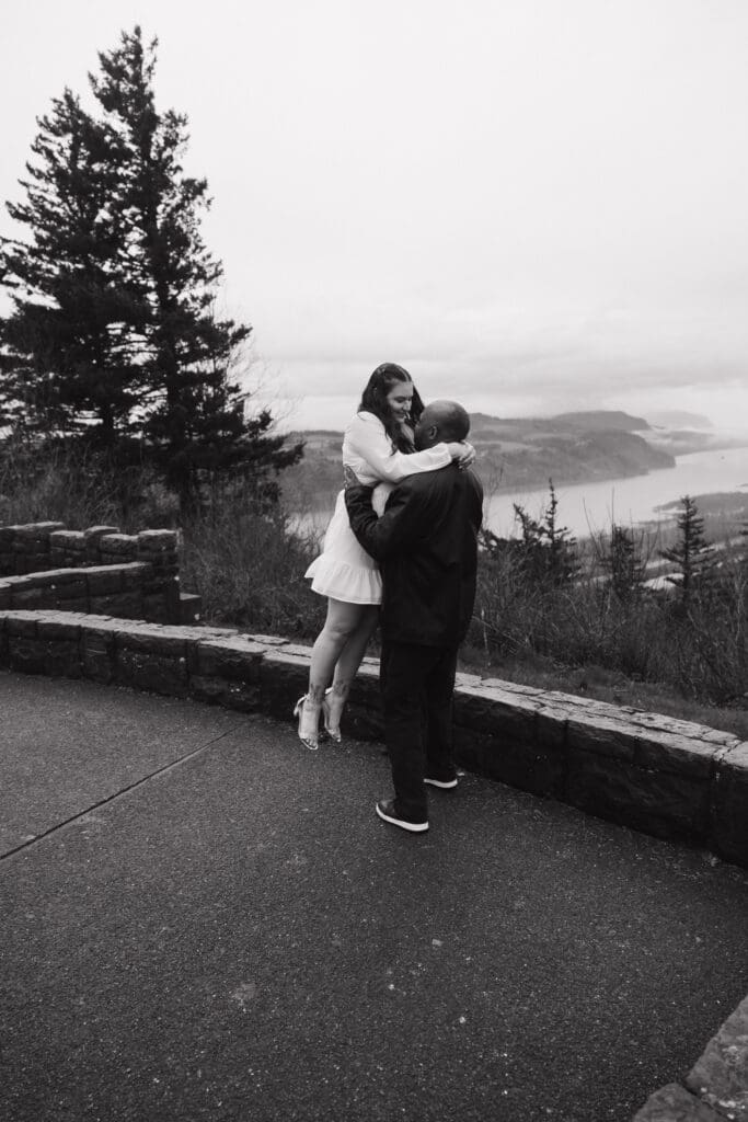 Black and white photo of couple lifted in embrace at Portland Women’s Forum State Scenic Viewpoint in Corbett, Oregon.