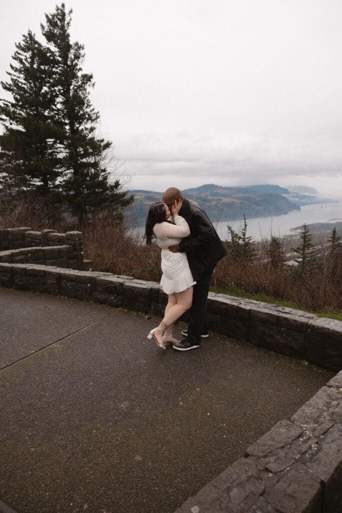 Couple kissing beside stone wall overlook at Portland Women’s Forum State Scenic Viewpoint in Corbett, Oregon.