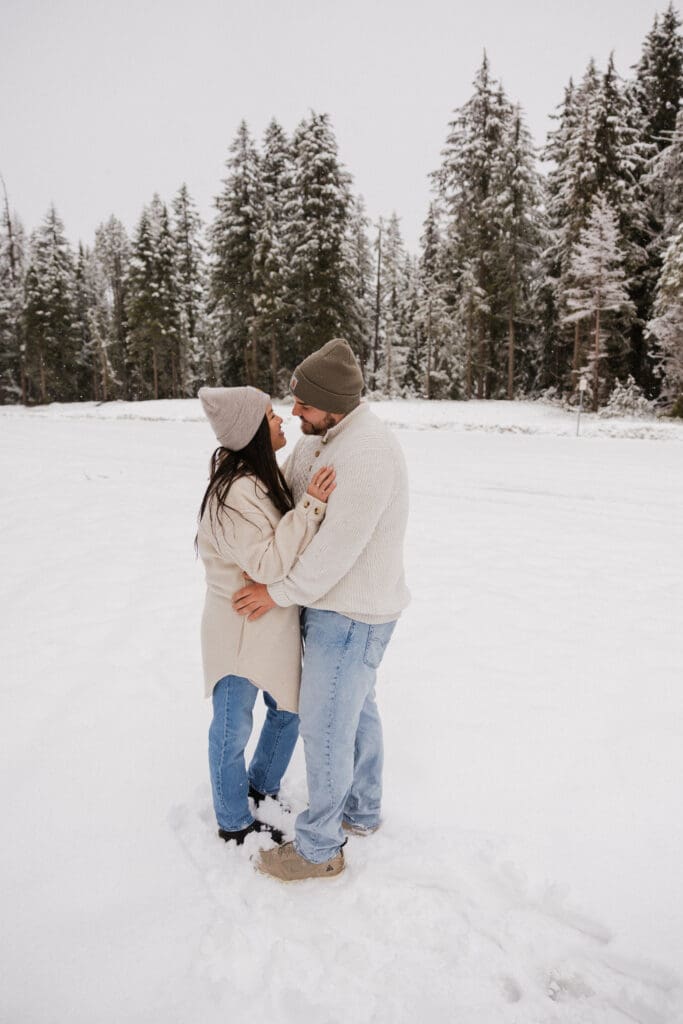 couple embracing in a snowy clearing in Mount Hood National Forest with winter forest and overcast sky behind them