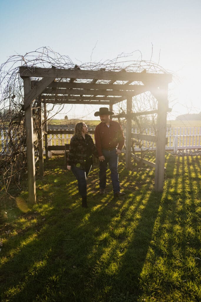 couple walking under vine covered wooden arbor during sunset engagement session at Champoeg State Park in Oregon