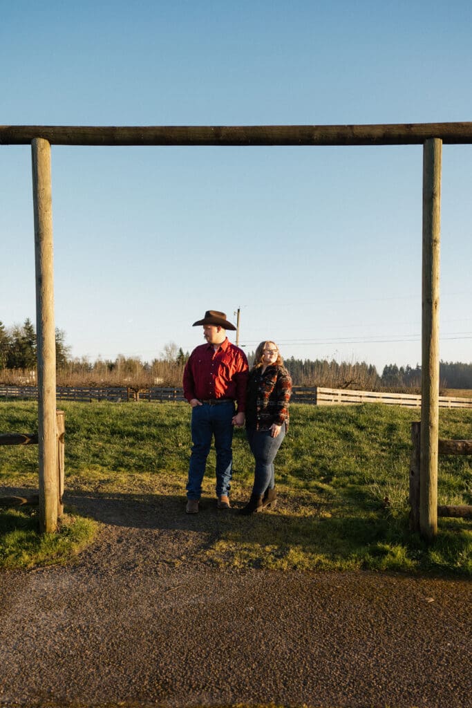 couple standing beneath wooden farm gate structure during engagement session at Champoeg State Park in Oregon