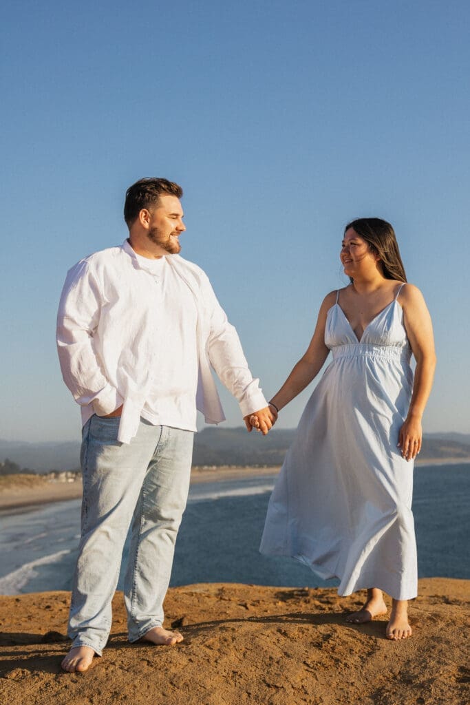Couple holding hands on an Oregon coast cliff for Pacific City, Oregon engagement session inspiration