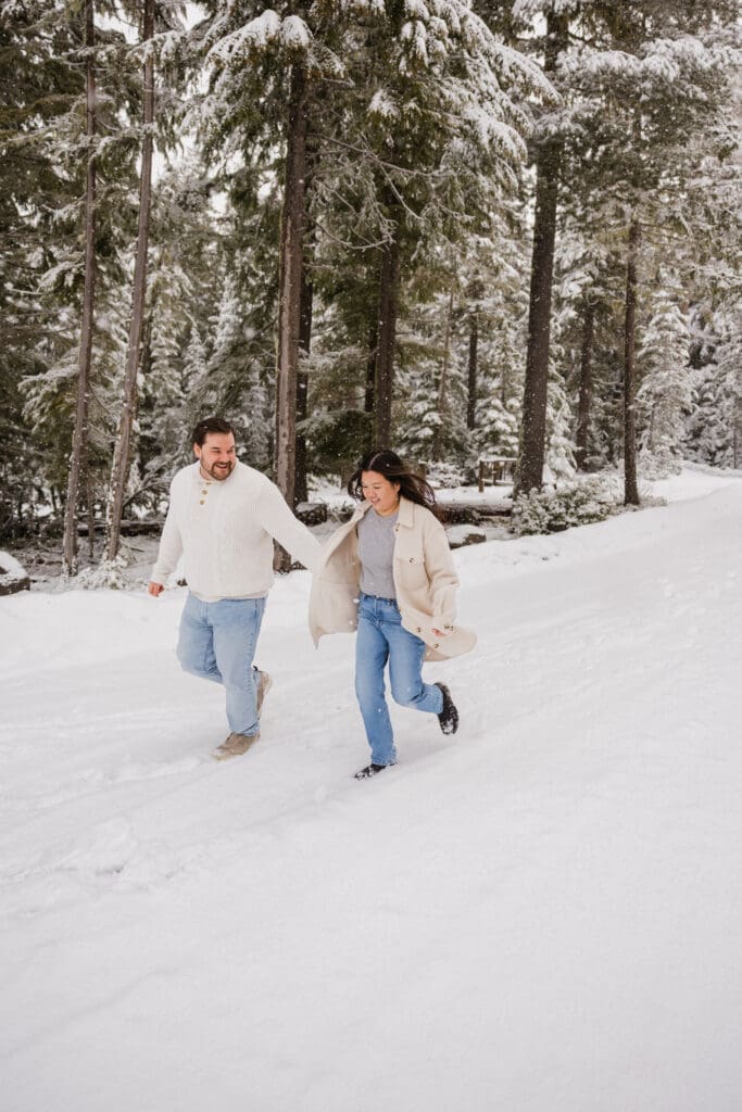 Couple running through snow-covered forest during a Mount Hood engagement session in Oregon
