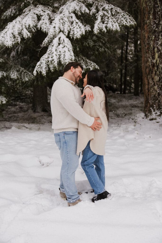 Couple embracing in the snow beneath pine trees during Mount Hood engagement photos in Oregon