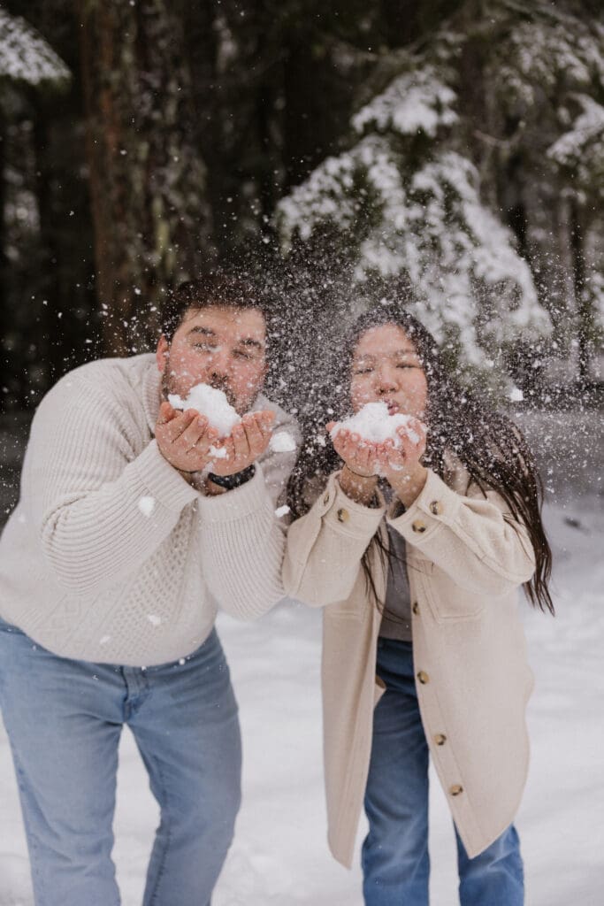 Couple blowing snow toward the camera during a playful Mount Hood engagement session in Oregon
