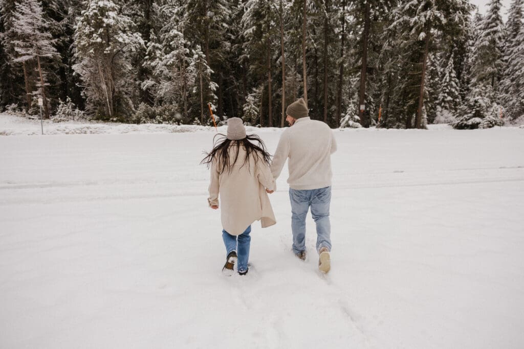 Couple walking across a snow-covered field during Mount Hood engagement photos in Oregon