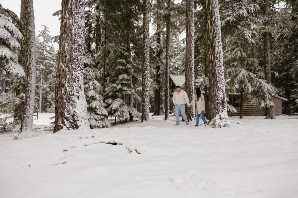 Couple walking through snowy forest near a cabin during a Mount Hood engagement session in Oregon