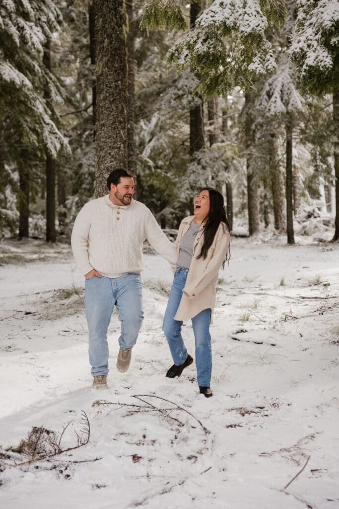 Couple holding hands and laughing in snowy woods during Mount Hood engagement photos in Oregon