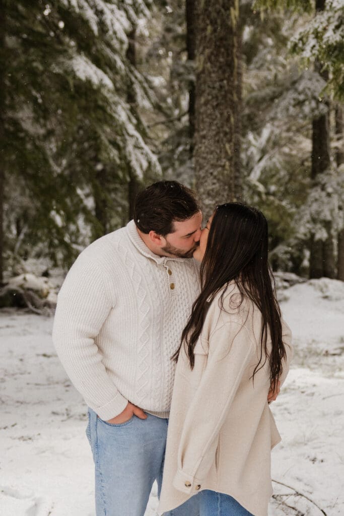 Couple kissing beneath snowy pine trees during a Mount Hood engagement session in Oregon