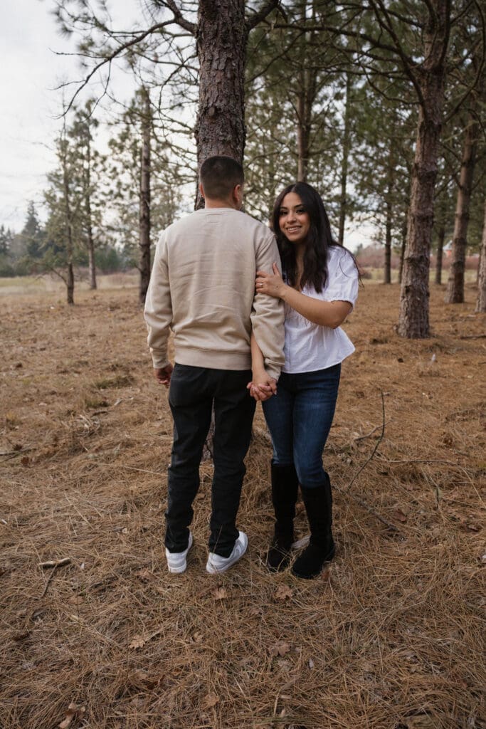 Couple holding hands beneath pine trees near Portland, Oregon for outdoor engagement photos