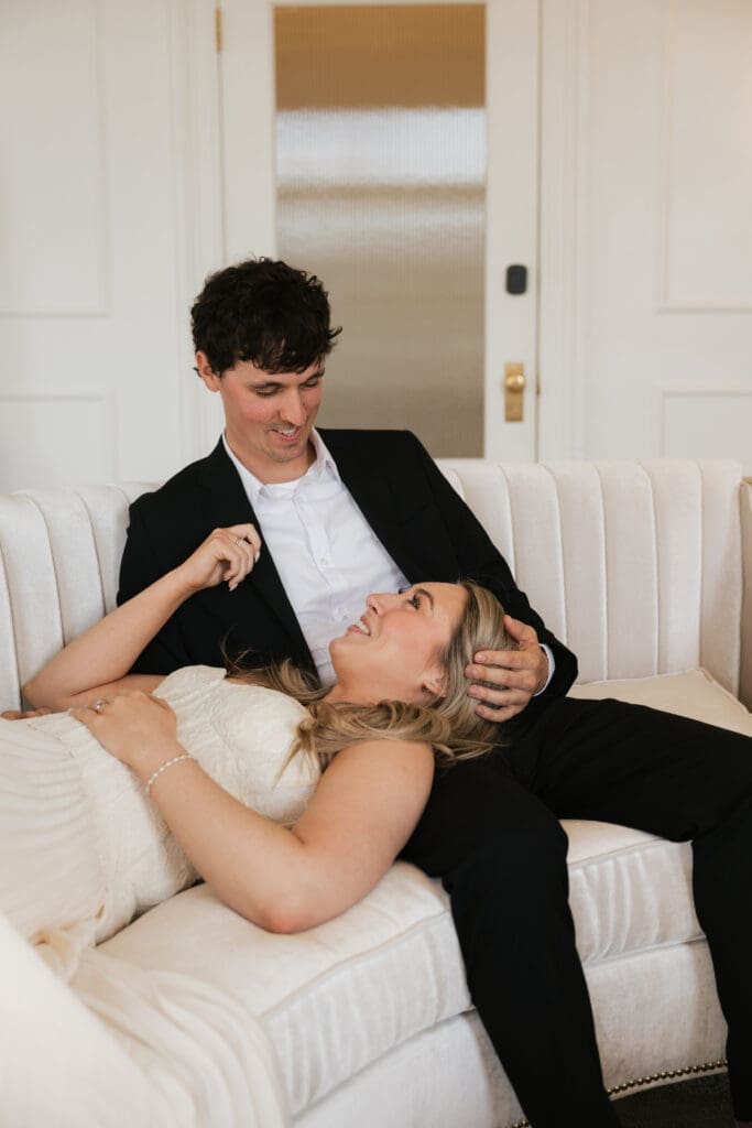 Couple smiling together on white couch during engagement session at The Arc Light in Oregon City, Oregon