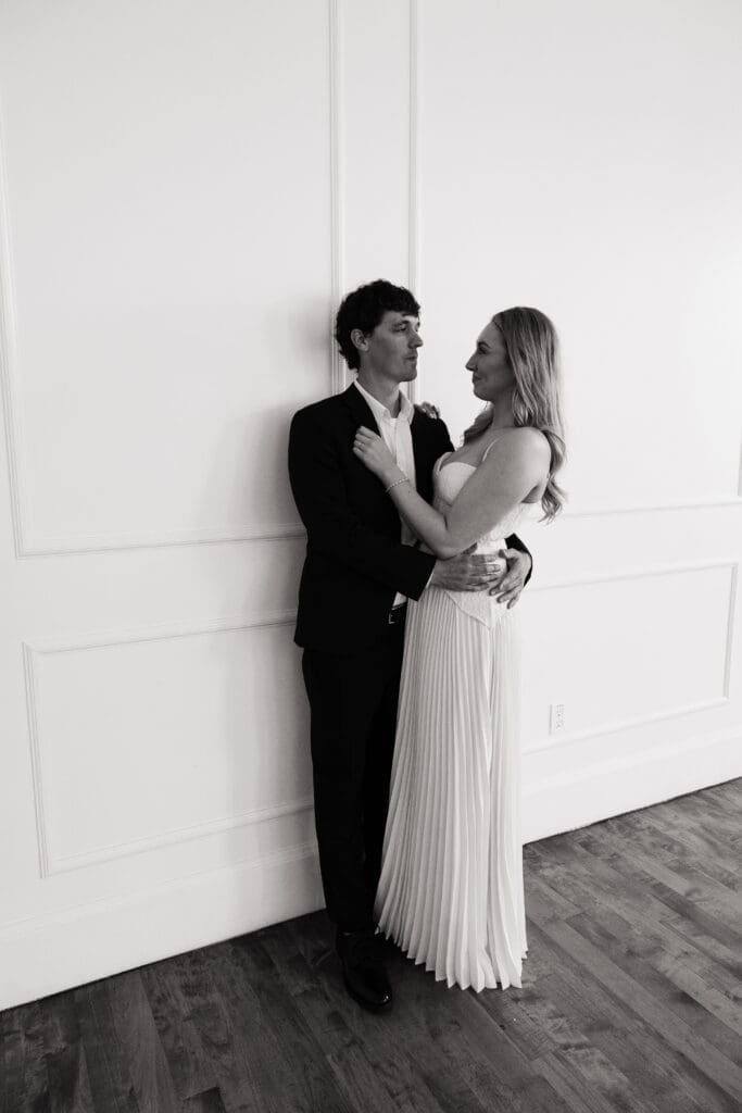 Black and white portrait of couple embracing against white wall at The Arc Light in Oregon City, Oregon