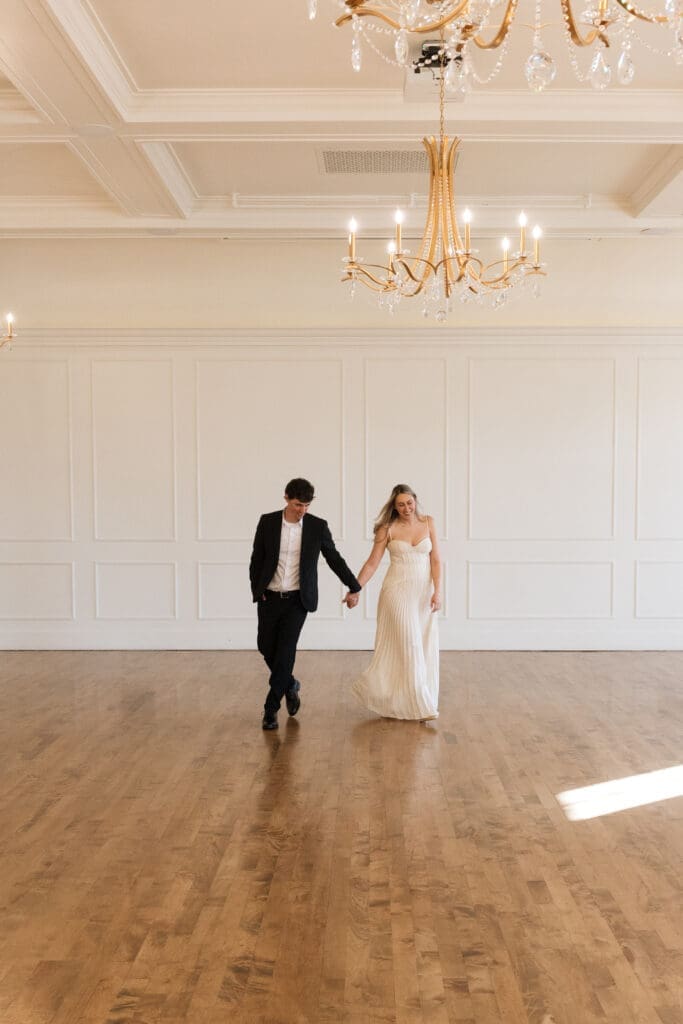 Couple walking hand in hand beneath chandeliers at The Arc Light in Oregon City, Oregon