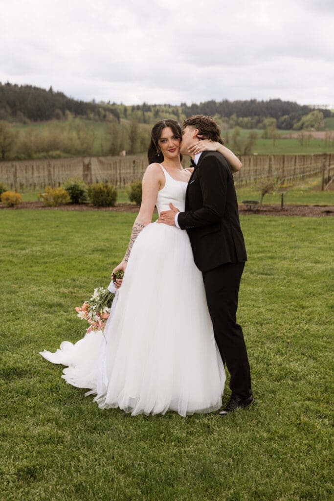 Bride and groom embracing on the lawn at The Farm on Golden Hill with vineyard rows in the background in Silverton Oregon