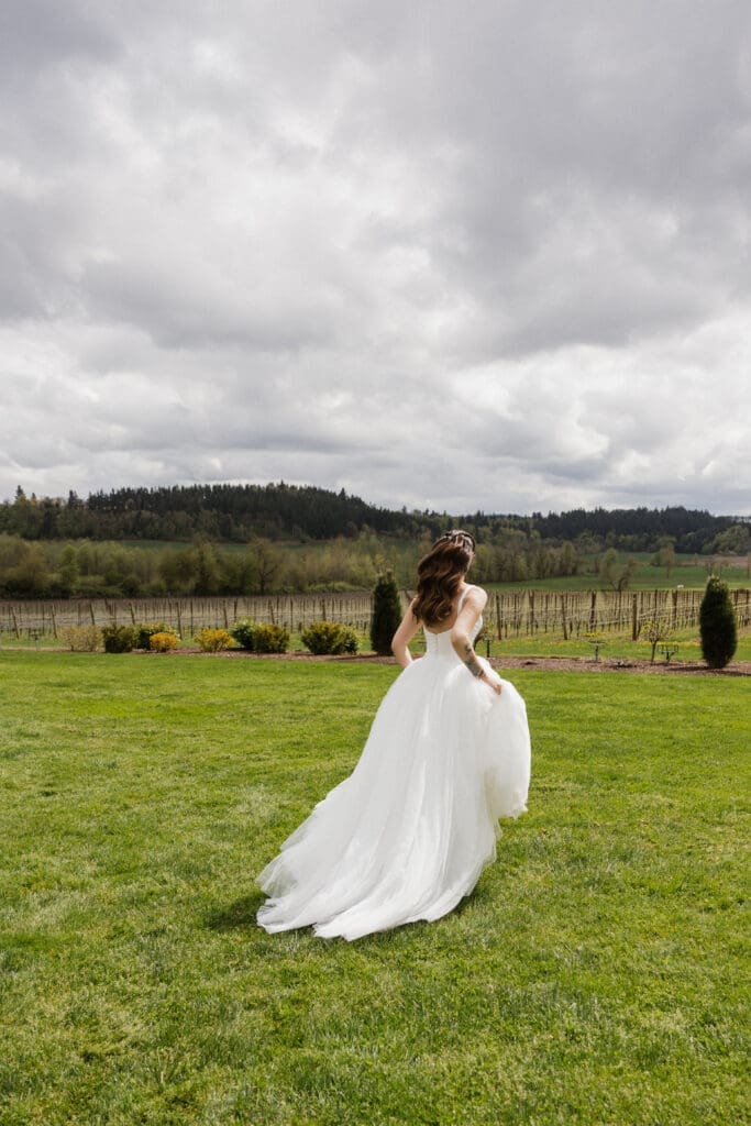 Bride in a white tulle gown walking toward the vineyard at The Farm on Golden Hill with dramatic Oregon sky in the background