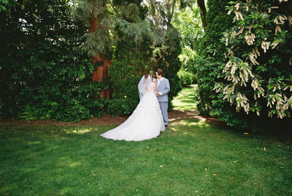Bride and bride share a quiet moment beneath towering trees during a film wedding at McMenamins Cornelius Pass Roadhouse in Hillsboro, Oregon.