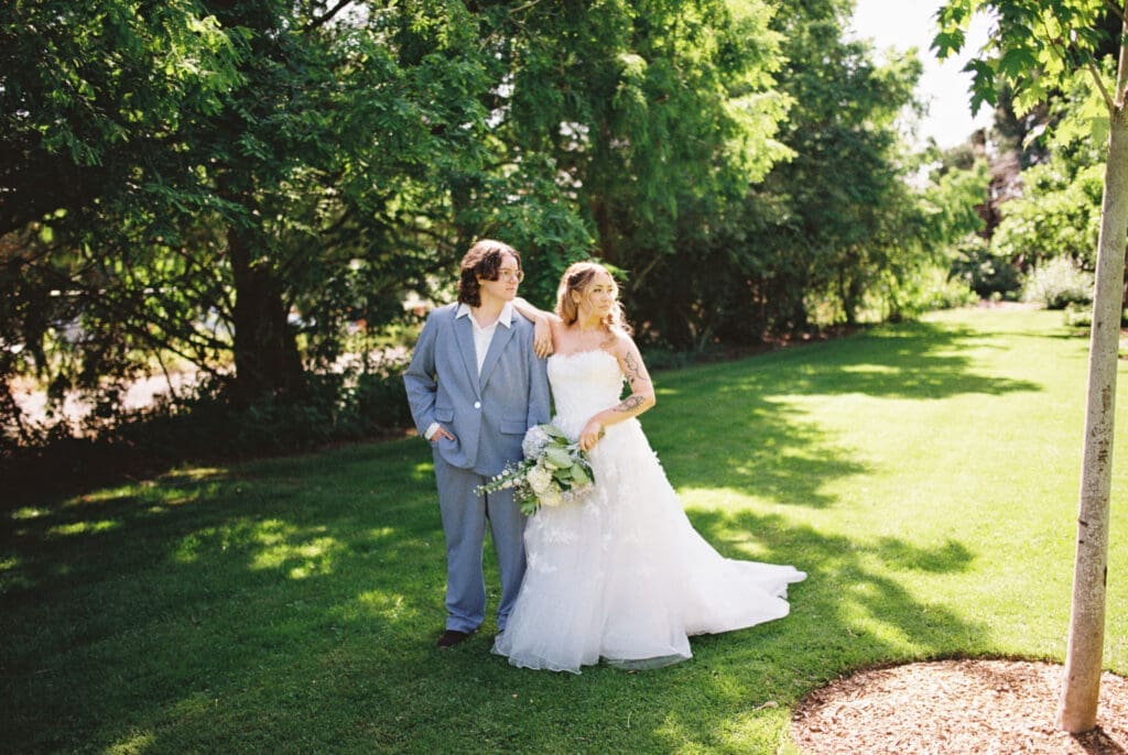 Bride and bride pose together on the lawn during a film wedding at McMenamins Cornelius Pass Roadhouse in Hillsboro, Oregon.