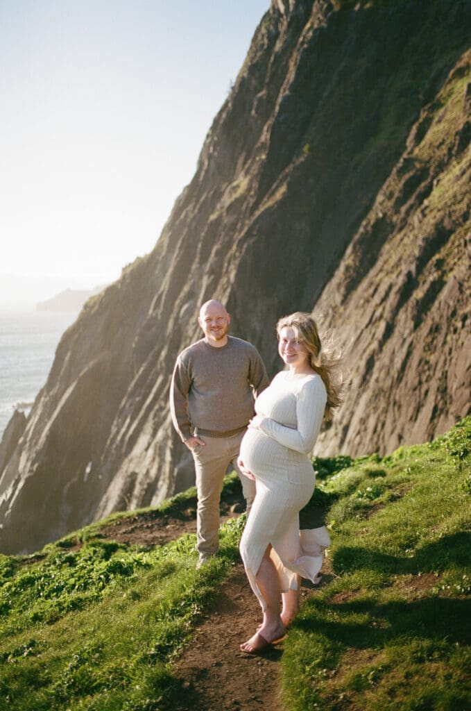 Pregnant couple standing on a grassy coastal bluff during a film maternity session at Cannon Beach, Oregon.