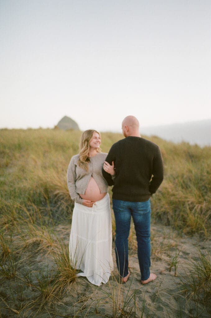 Pregnant couple standing together in beach grass during a film maternity session at Cannon Beach, Oregon.