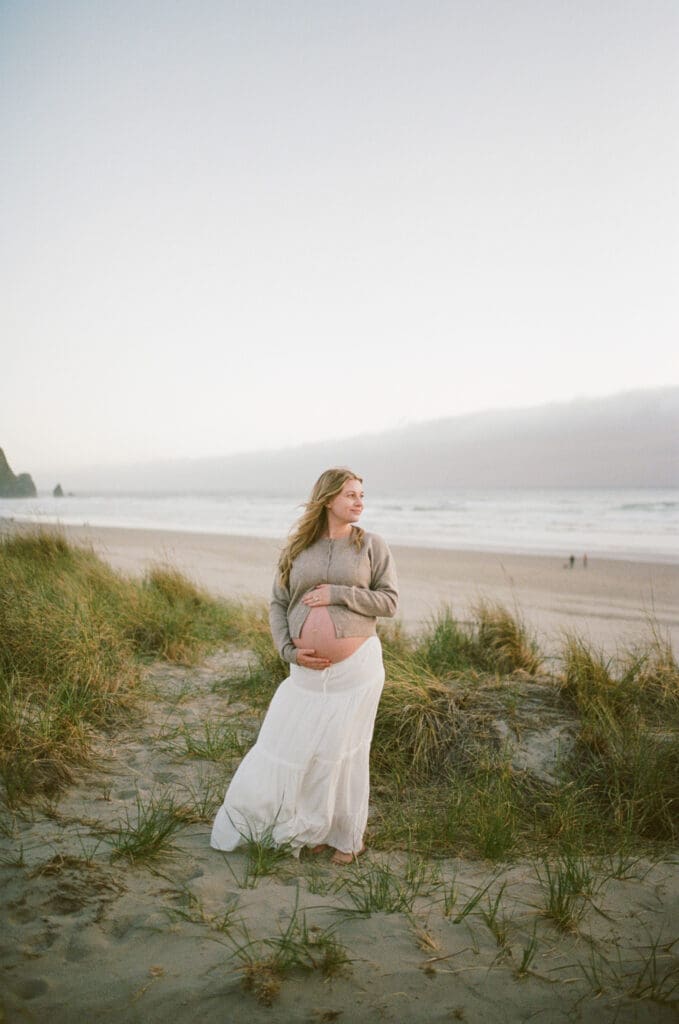 Pregnant person posing among coastal dunes during a film maternity session at Cannon Beach, Oregon.