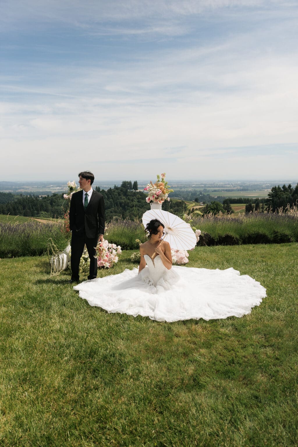 Bride seated with a parasol beside groom in the gardens at Black Walnut Inn in Dundee, Oregon.