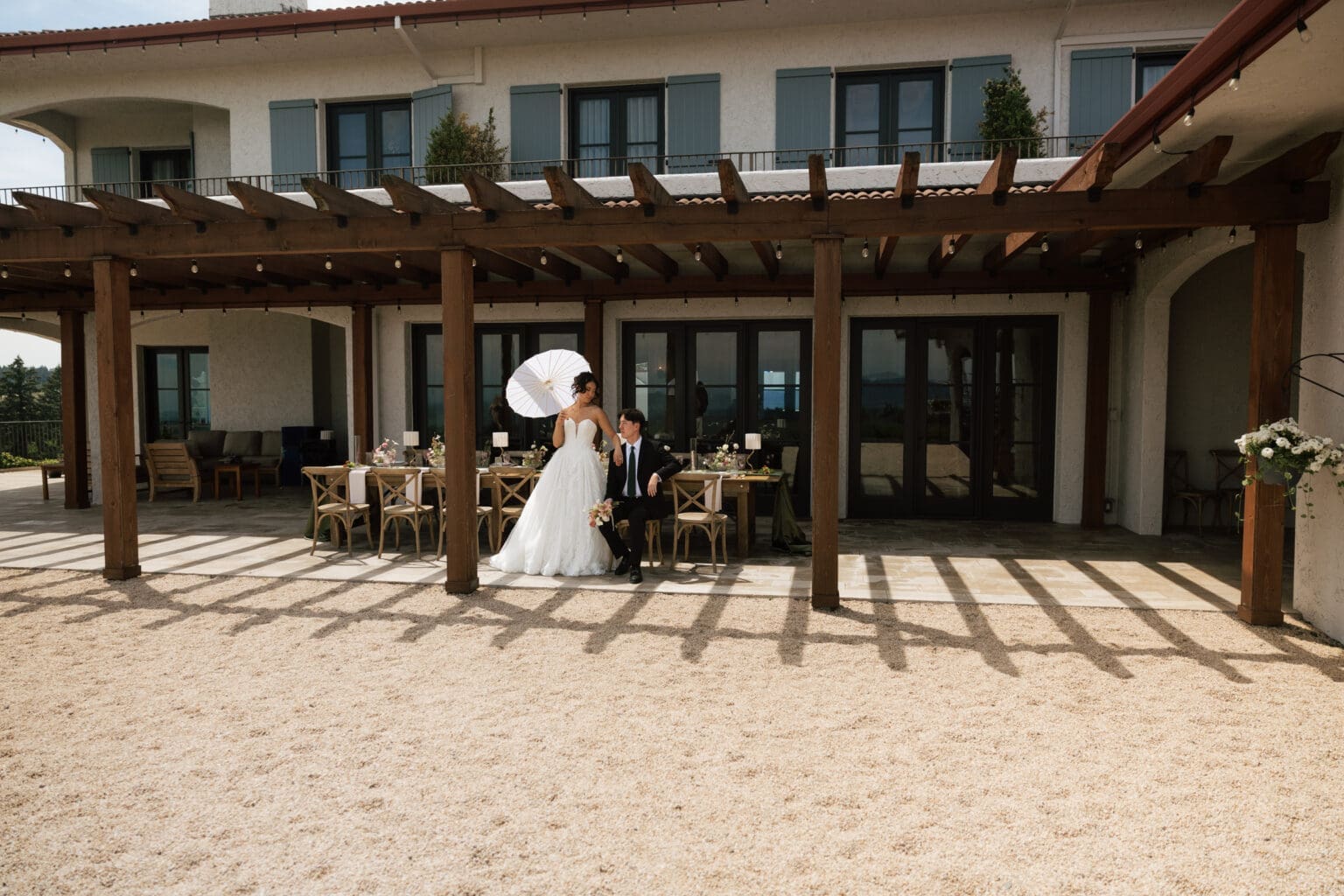 Couple posing beneath the pergola outside Black Walnut Inn in Dundee, Oregon with reception tables behind them.