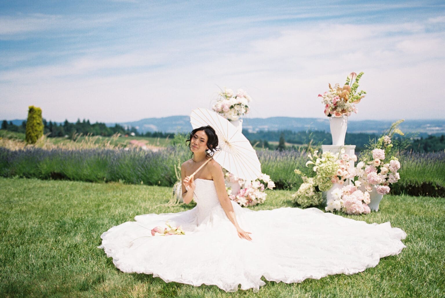 Film photograph of the bride seated with a white parasol before floral ceremony arrangements at Black Walnut Inn in Dundee, Oregon.